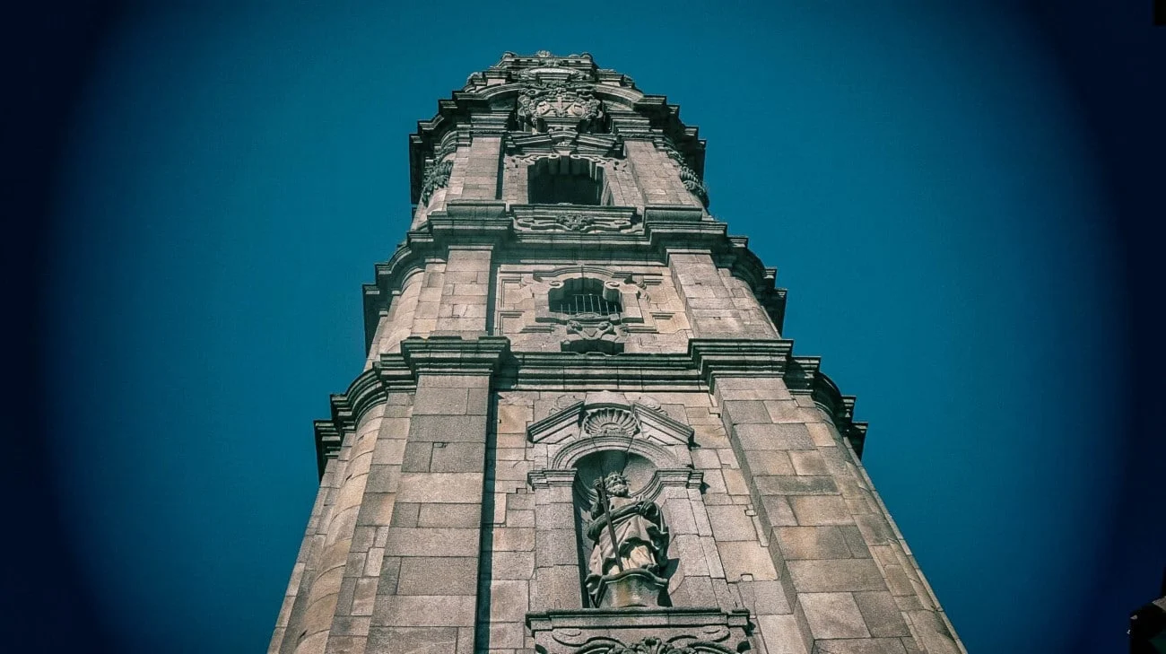 Looking straight up at the Torre dos Clérigos with a saint statue in a niche