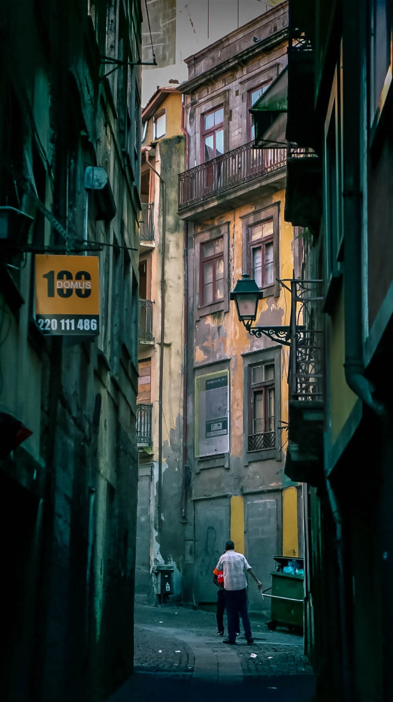 A man walking through a narrow, dimly-lit alley between weathered old buildings