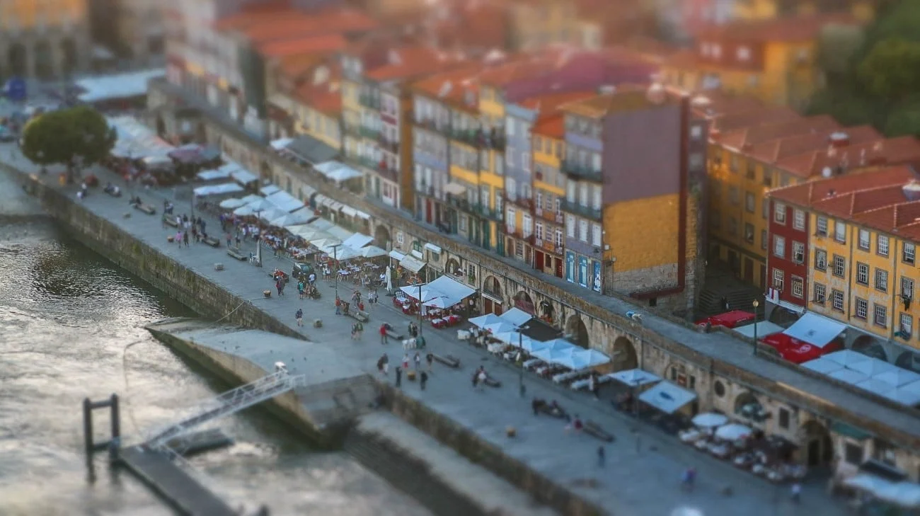 Tilt-shift close-up of the Ribeira promenade with restaurant umbrellas and colorful buildings