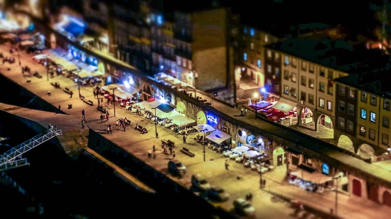 Tilt-shift nighttime view of the Ribeira waterfront with glowing restaurants