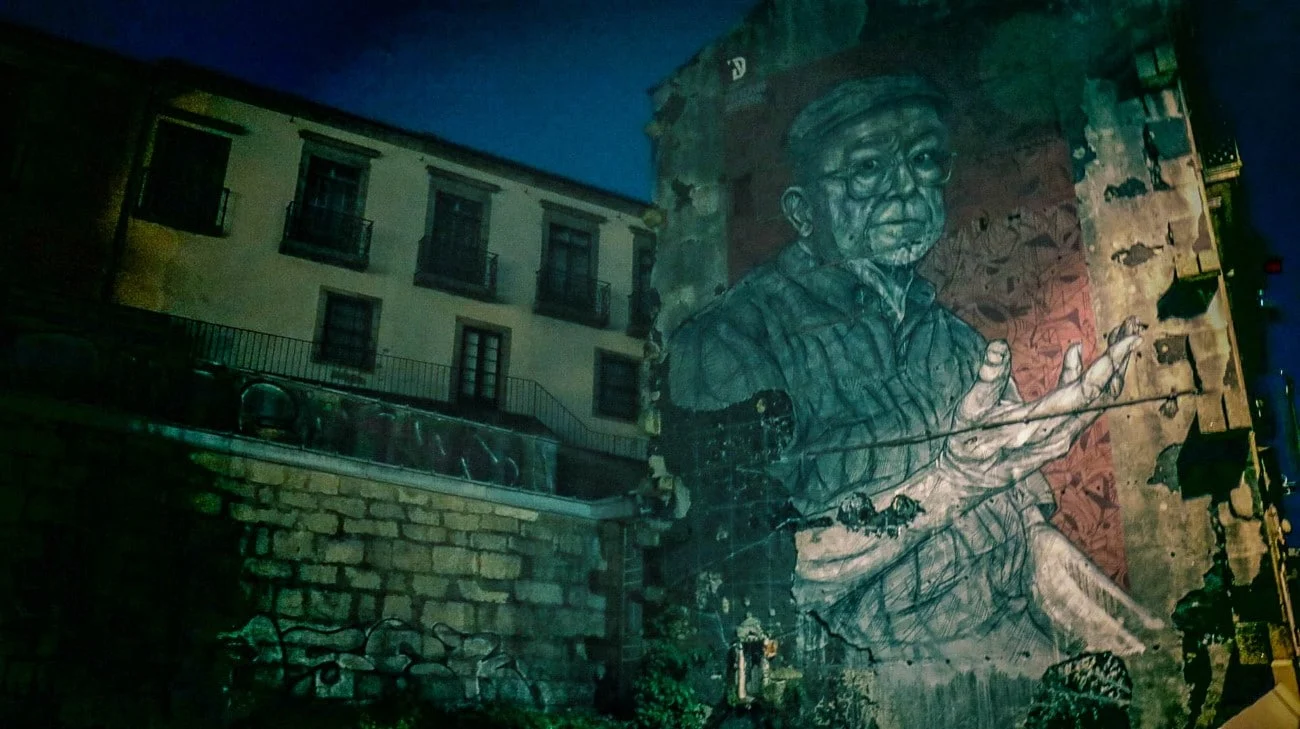 A large street art mural of an elderly man on the side of a building at night