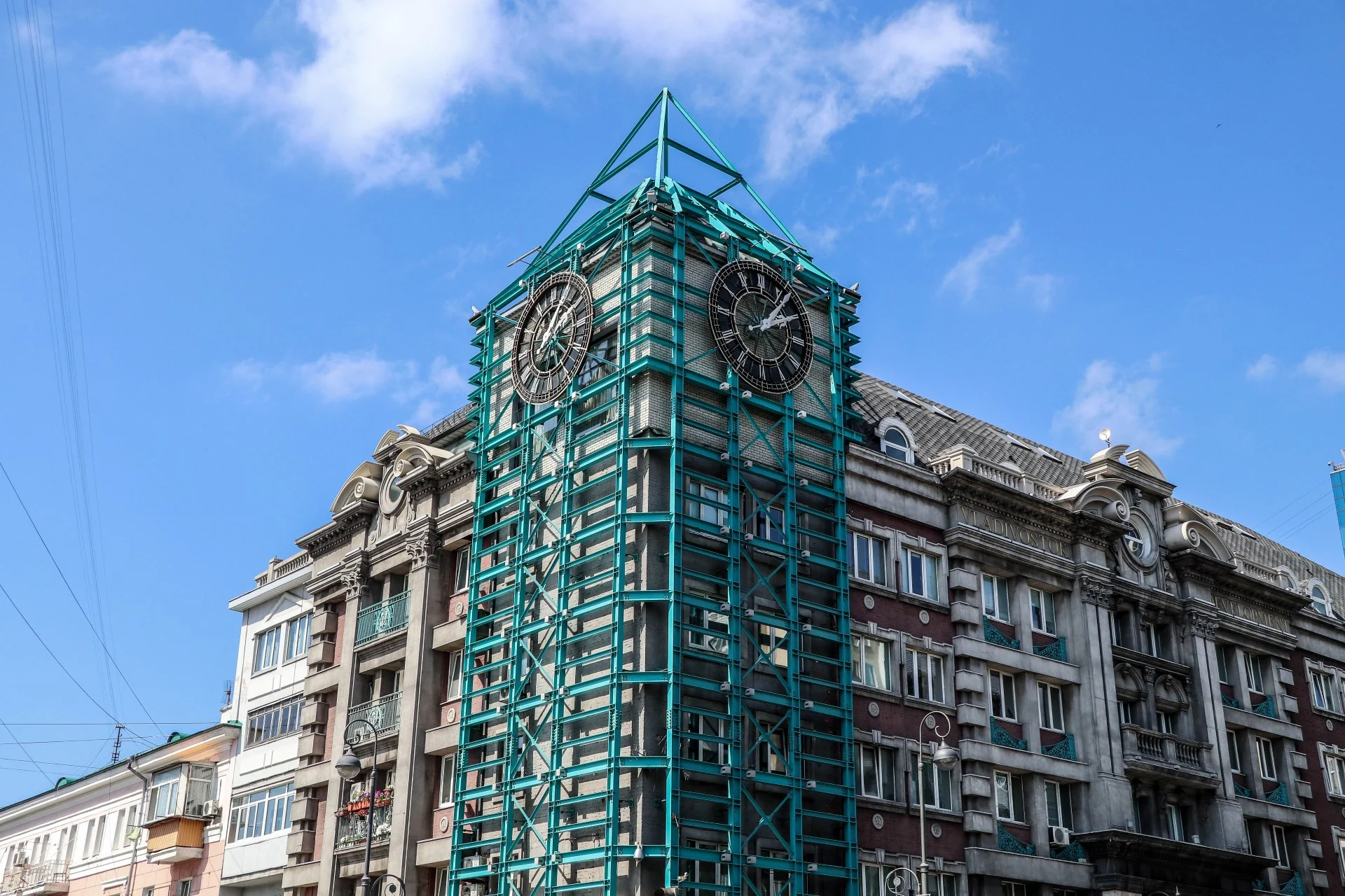 A clock tower wrapped in turquoise scaffolding for restoration