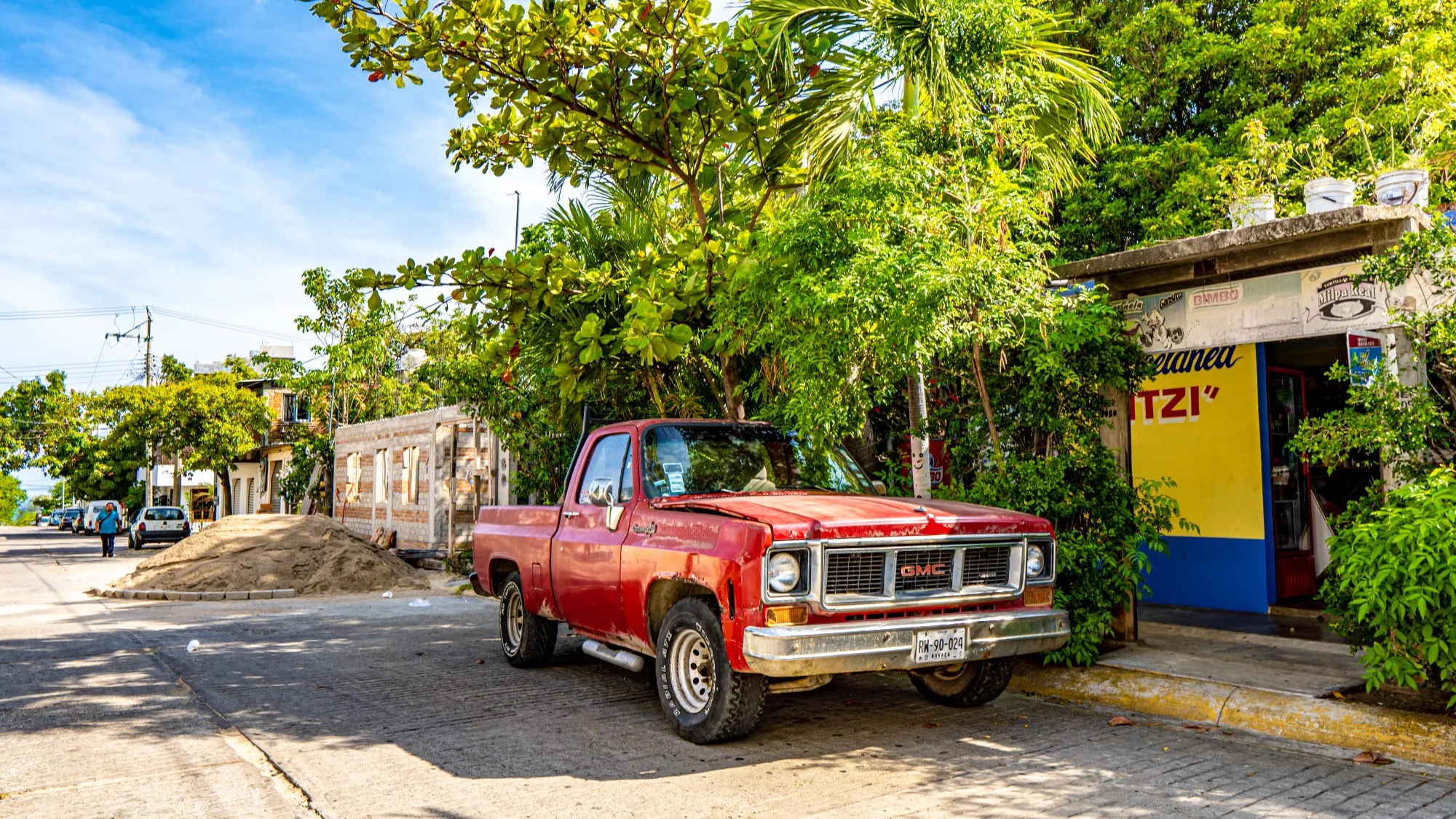 An old red truck sits idle under the hot Puerto Escondido sunshine