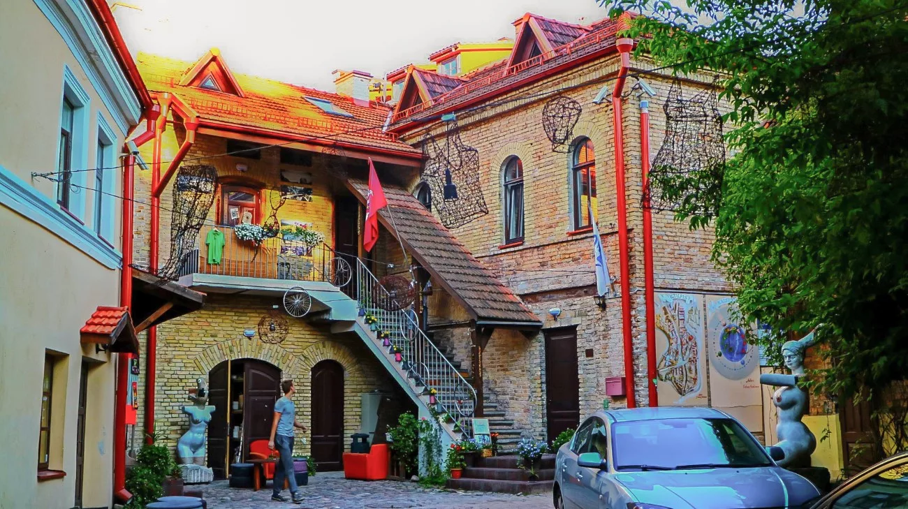 An eclectic courtyard with metal sculptures and a pink flag in Uzupis