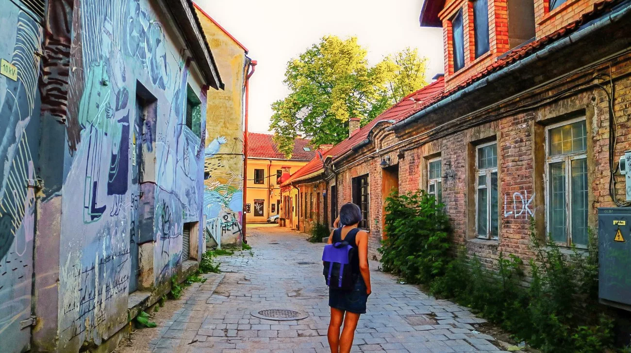 A woman walking down a graffiti-lined alley of weathered brick in Uzupis