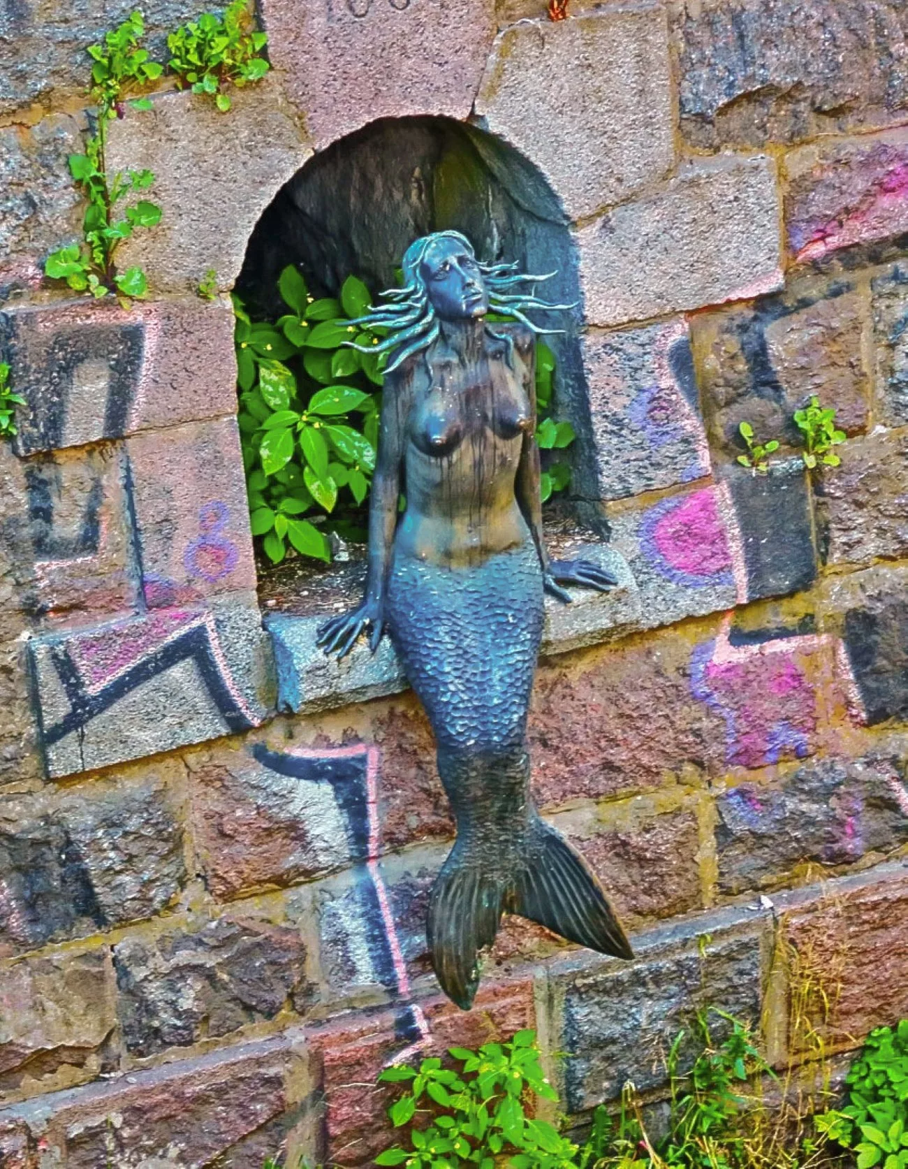 A bronze mermaid sculpture set into a stone wall niche in Uzupis