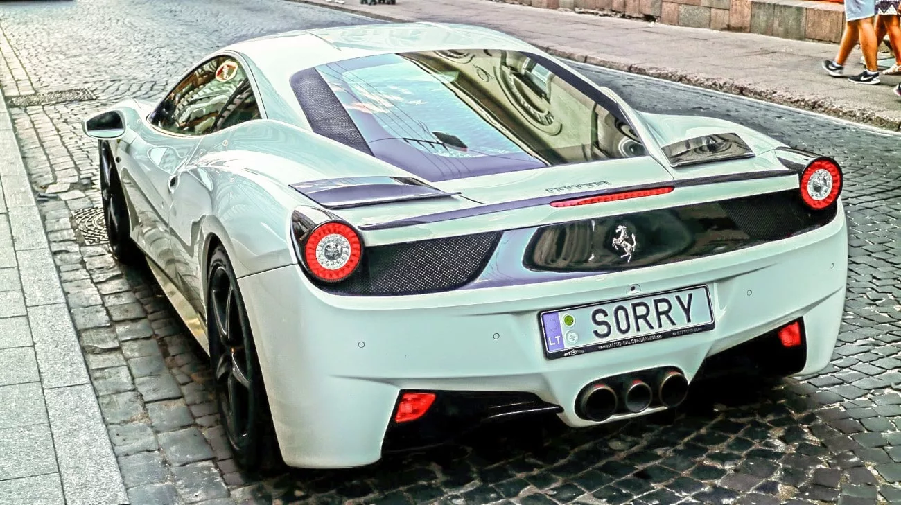 A white Ferrari 458 with a SORRY vanity plate on the cobblestones