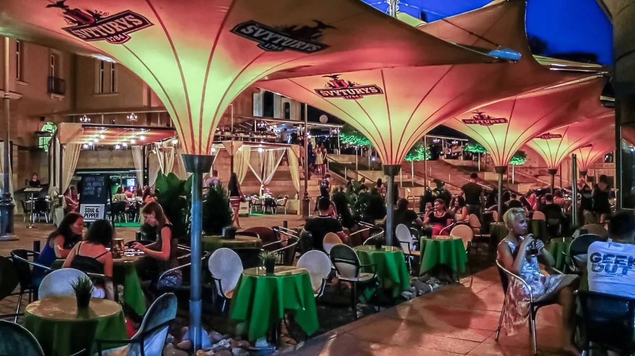 Outdoor bar scene under glowing Svyturys parasols on a summer night