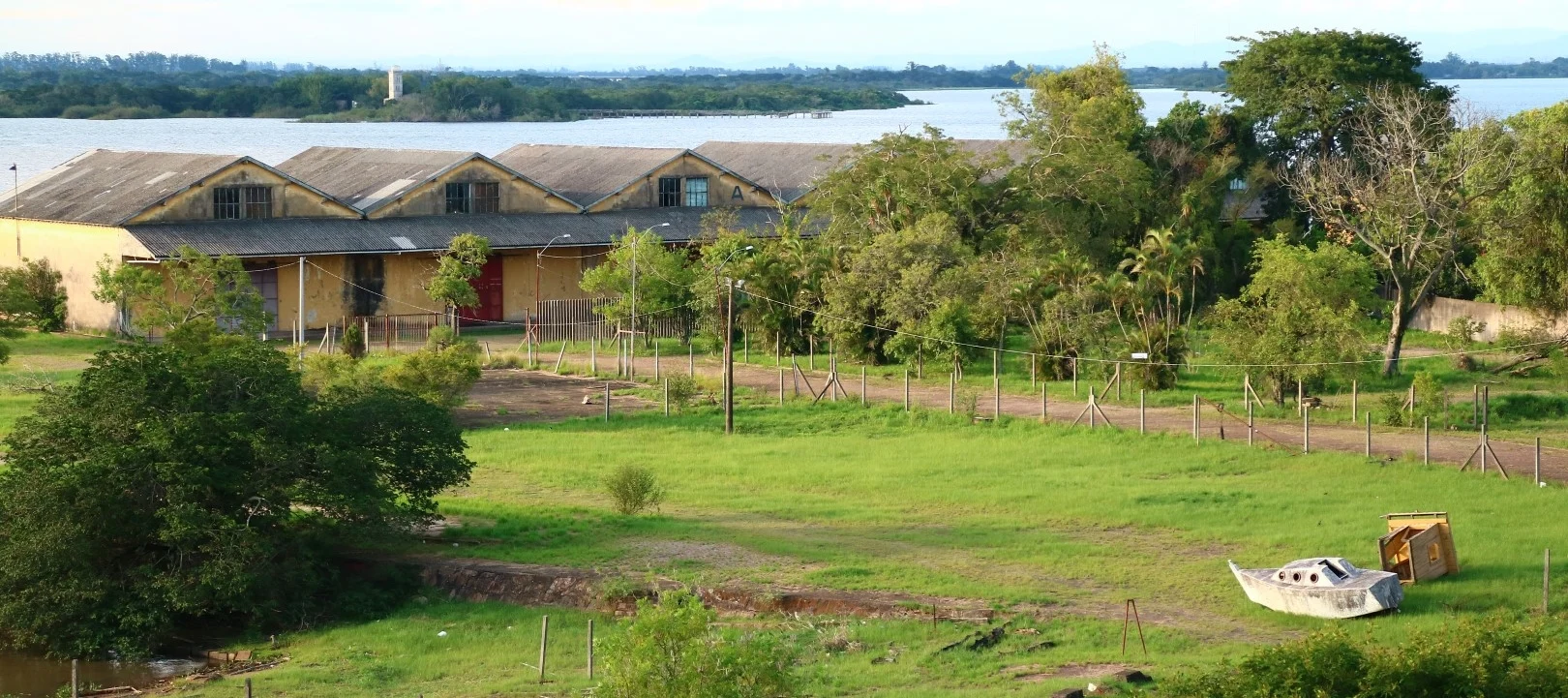 The Cais Mauá: long pitched-roof warehouses on the Guaíba river, a wrecked sailboat abandoned in the grass.